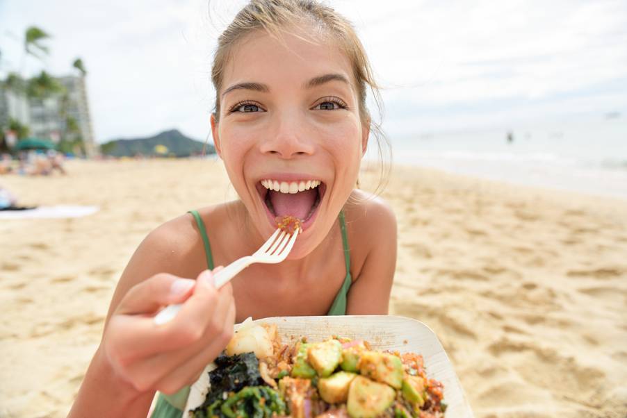 Ragazza che mangia un piatto di insalata in spiaggia